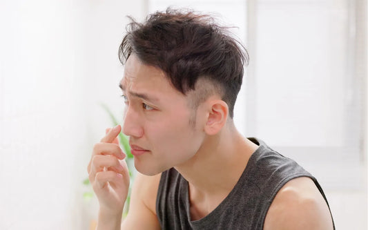 Young man in front of a mirror experiencing a breakout and a bad skin day