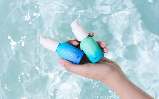 Hand holding PSA skincare bottles over water, highlighting products that contain must-have summer skincare ingredients