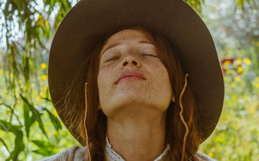 redhead freckled girl with a hat sunbathing while wondering about what causes freckles